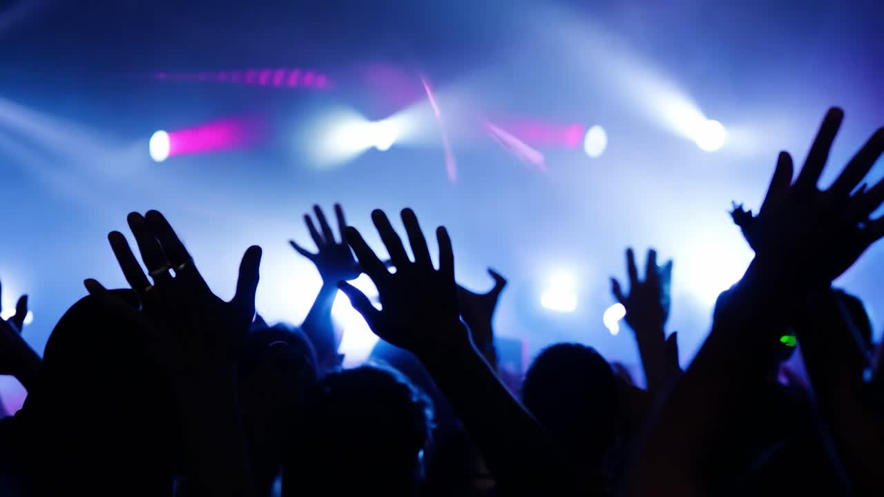 Excited music fans cheer with arms raised, creating an electrifying atmosphere at a lively concert
