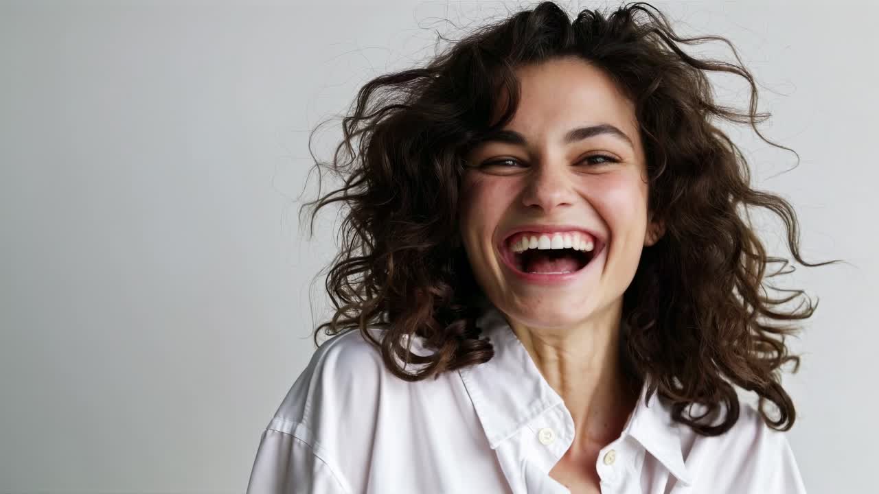 A joyful woman with curly hair laughs in a close-up shot. The video captures her in a natural