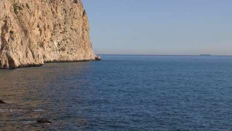 Sea-cliffs-with-calm-blue-ocean-and-ship-on-horizon,-mediterranean-Spain