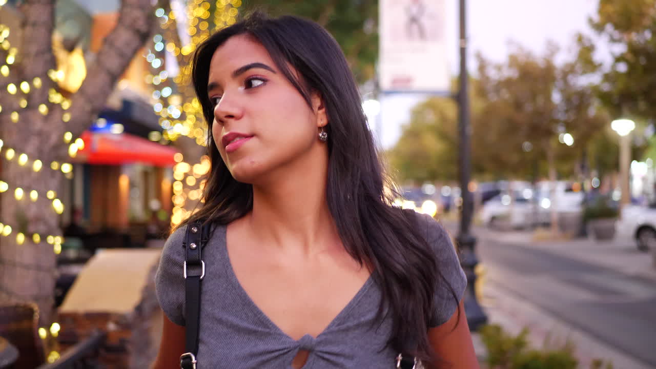una atractiva joven hispana caminando por una calle del centro de la ciudad en california con restaurantes, tiendas y tiendas minoristas con luces a cámara lenta