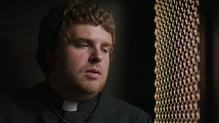 Sacerdote che parla con un fedele attraverso una grata durante la confessione