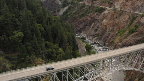 drone pull back view going over an extremely tall metal bridge spanning another smaller bridge and a river. cars pass on bridge.
