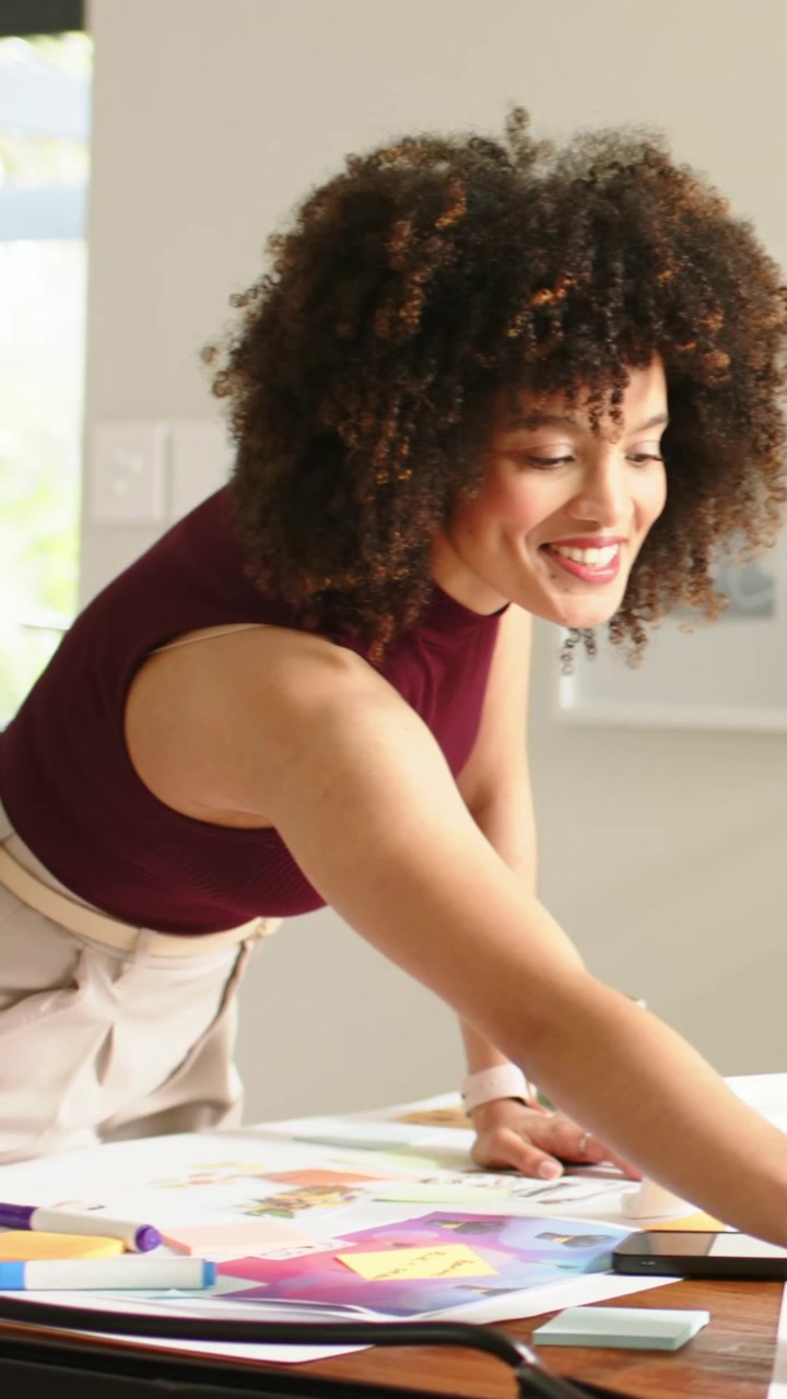 Vertical video: Starting layout, woman in maroon top arranging sheets, sticky notes in home studio