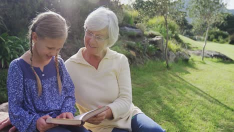 Grandmother-and-little-girl-sitting-on-a-grass-and-reading-book-4K-4k