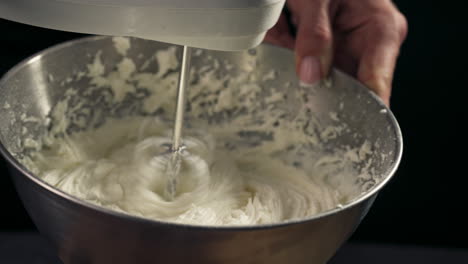 hand holds bowl and mixer at angle to combine all ingredients into a whipped frosting, slow motion