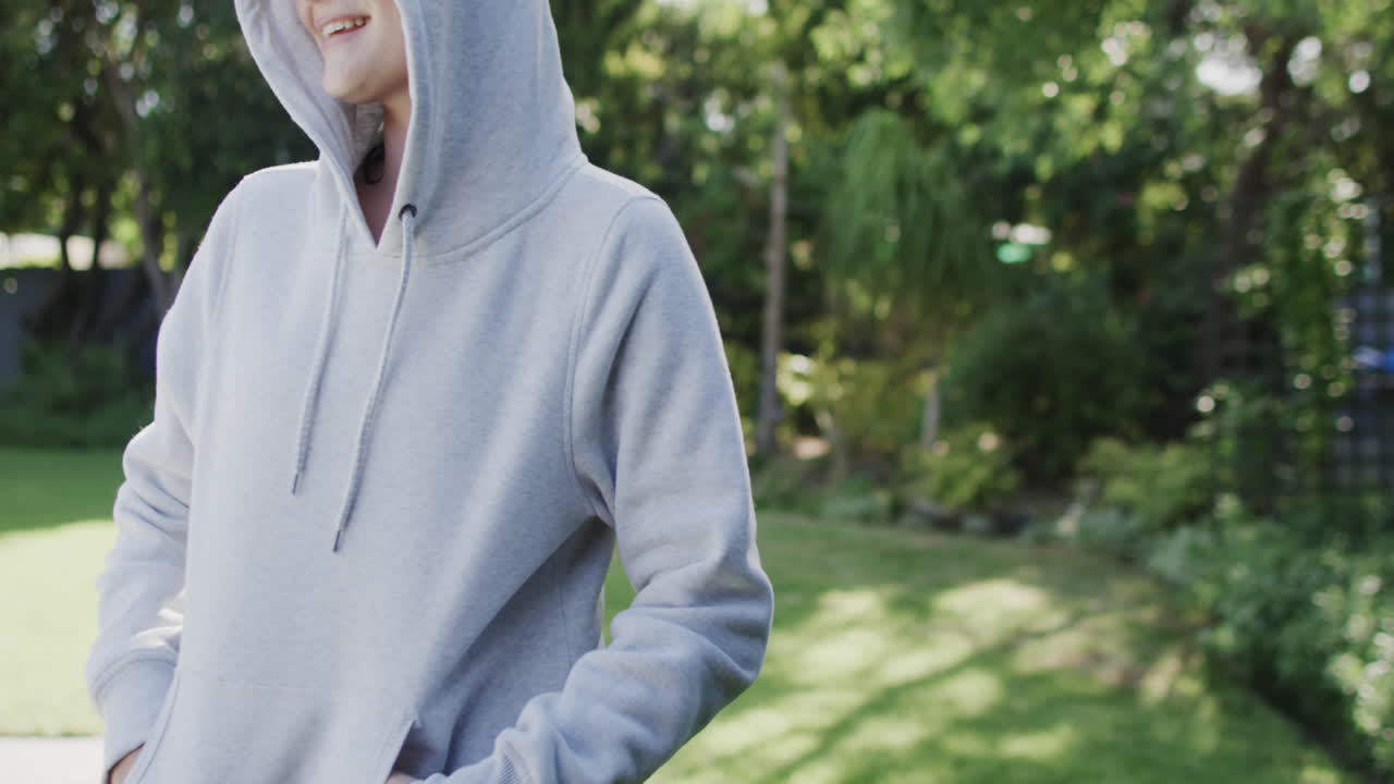 Happy caucasian woman in white hooded top in sunny garden in slow motion with copy space