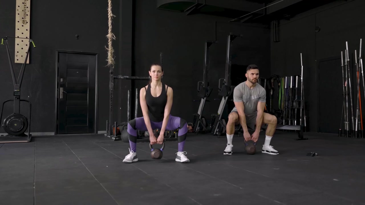 Uomo e donna che eseguono squat con kettlebell in palestra
