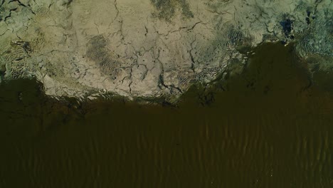 Drone-bird's-eye-view-static,-ripples-of-green-toxic-water-float-by-refuse-run-off-asphalt-lake