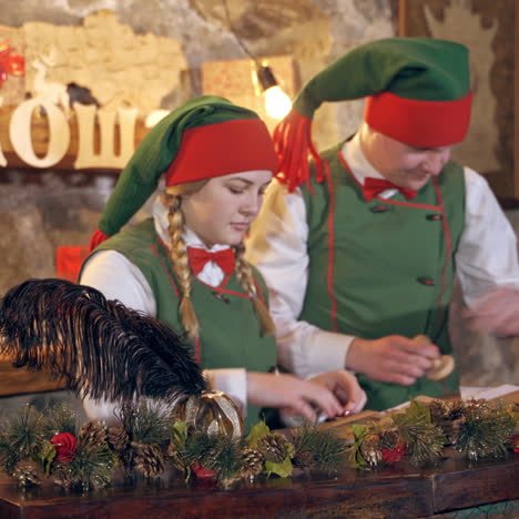 elves with envelopes. fairy characters in green costumes with letters at christmas time. female elf holding black feather on christmas gifts background.