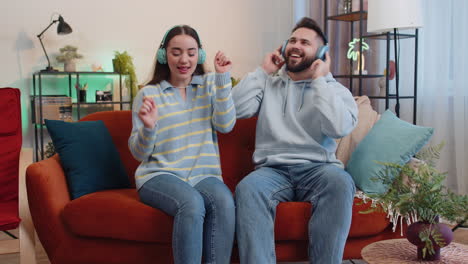 Hombre-De-Familia-Mujer-Con-Auriculares-Inalámbricos-Bailando-Escuchando-Música-Rock-N-Roll-Favorita-En-El-Sofá-De-Casa