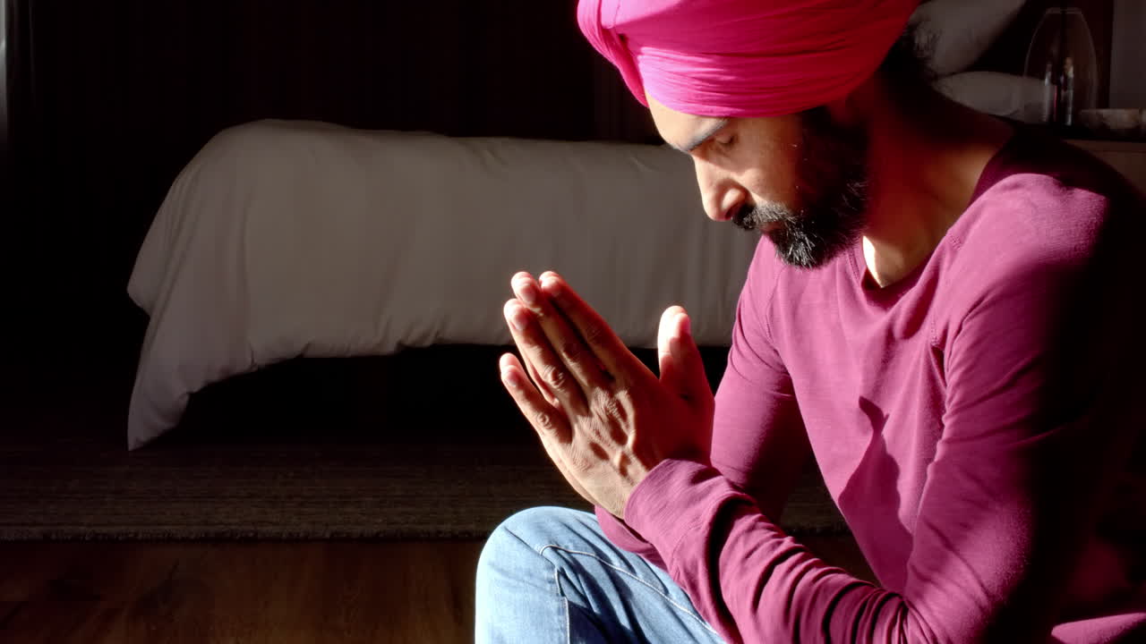 Praying, man in traditional turban sitting cross-legged in bedroom