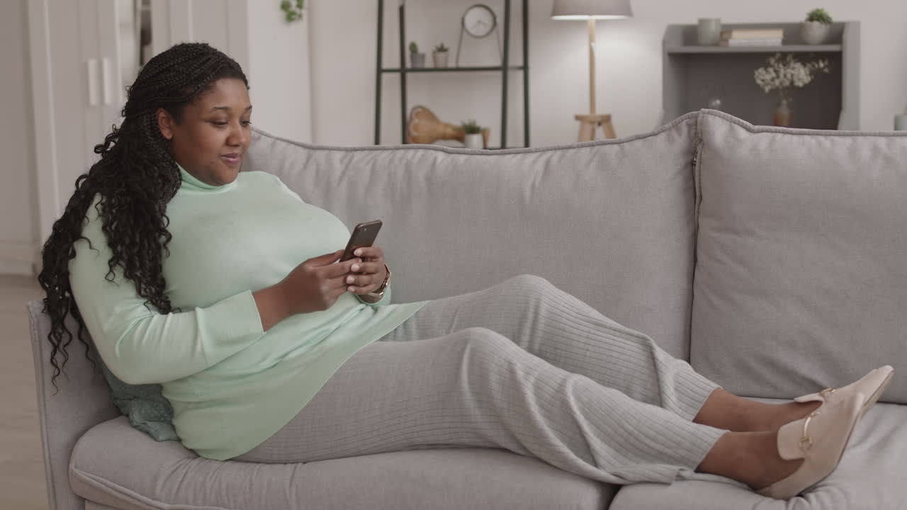 Young Woman Lying on Sofa and Using Smartphone