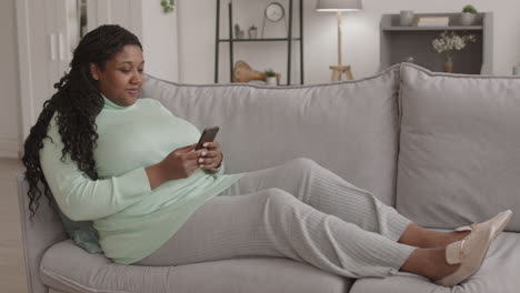 young woman lying on sofa and using smartphone