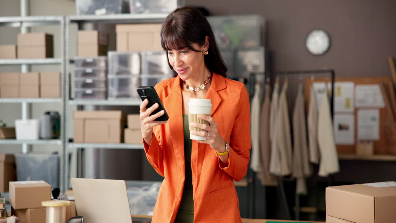 Donna felice che usa lo smartphone e beve caffè in un ufficio di piccola impresa