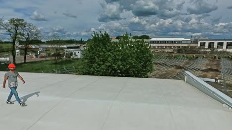technician in orange helmet on the roof. worker goes on a flat roof of industrial building on the background of a construction of a new solar farm. aerial view.