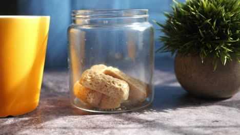 biscotti en un frasco de vidrio con una taza y una planta