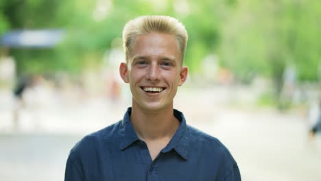 Close-up-portrait-young-happy-blond-man-standing-in-nature-between-park-trees-relaxes,-breathes-fresh-air.-Male-enjoys-a-life-of