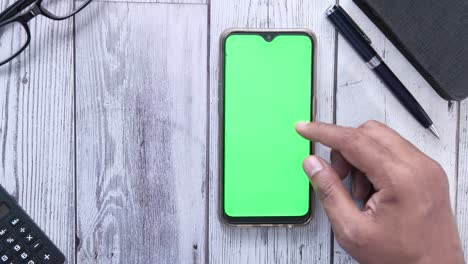 hand touching a smartphone with a green screen on a wooden table