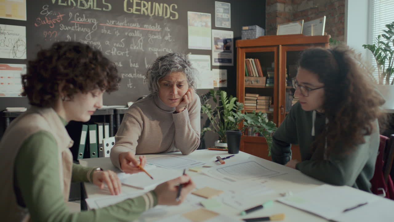 Teacher and Two Students Discussing Text on Papers during English Lesson