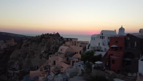 Imágenes-Aéreas-De-Oia,-Las-Famosas-Casas-Blancas-De-Santorini-Y-Cúpulas-Azules-En-El-Borde-Del-Acantilado-Y-La-Laguna-Azul