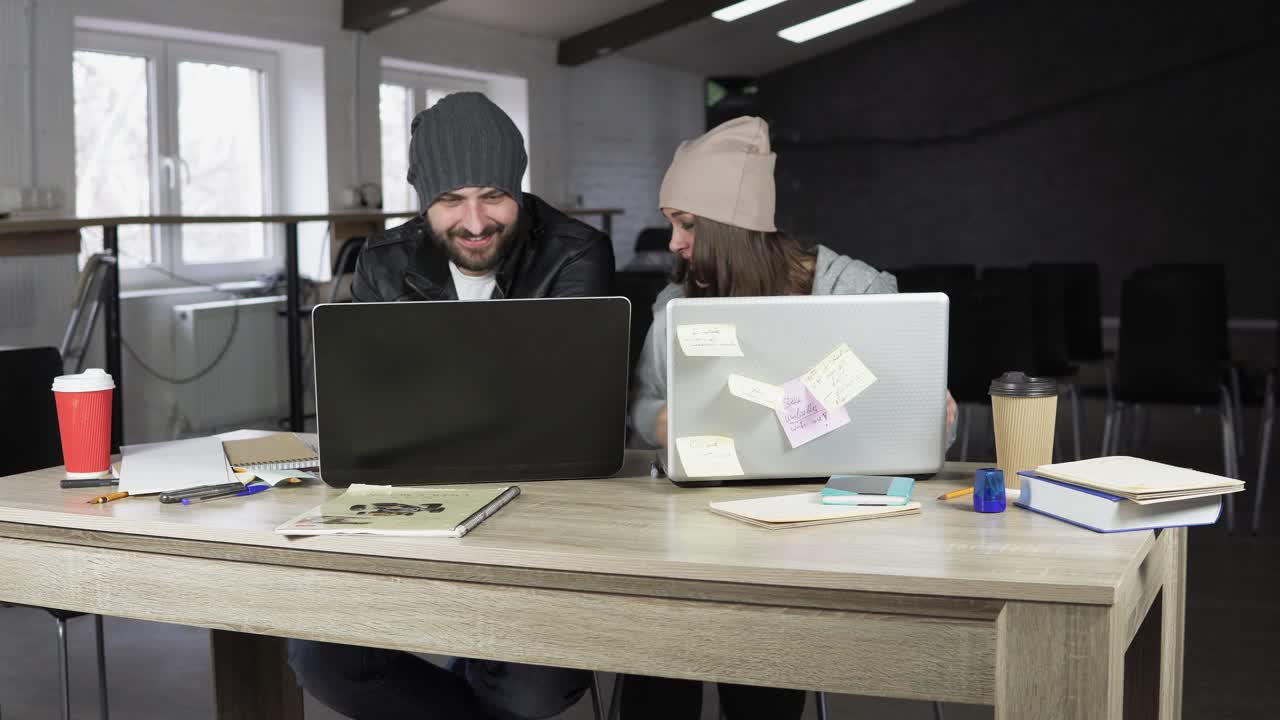 Young man and woman working in creative office. White and black laptops on the table. Modern design of the office. Shot in 4k