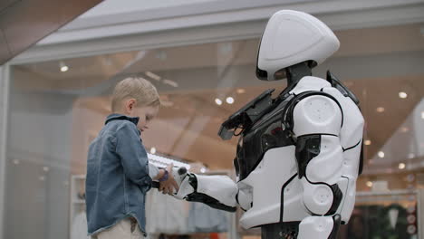 the boy stretches out his hand to the robot for a handshake