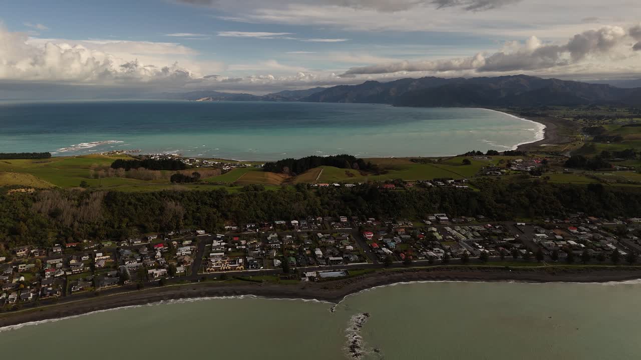 Kaikoura area with residential area and city during cloud. Sunset. Turquoise ocean water in fore and background. Coastline of New Zealand. Drone wide shot