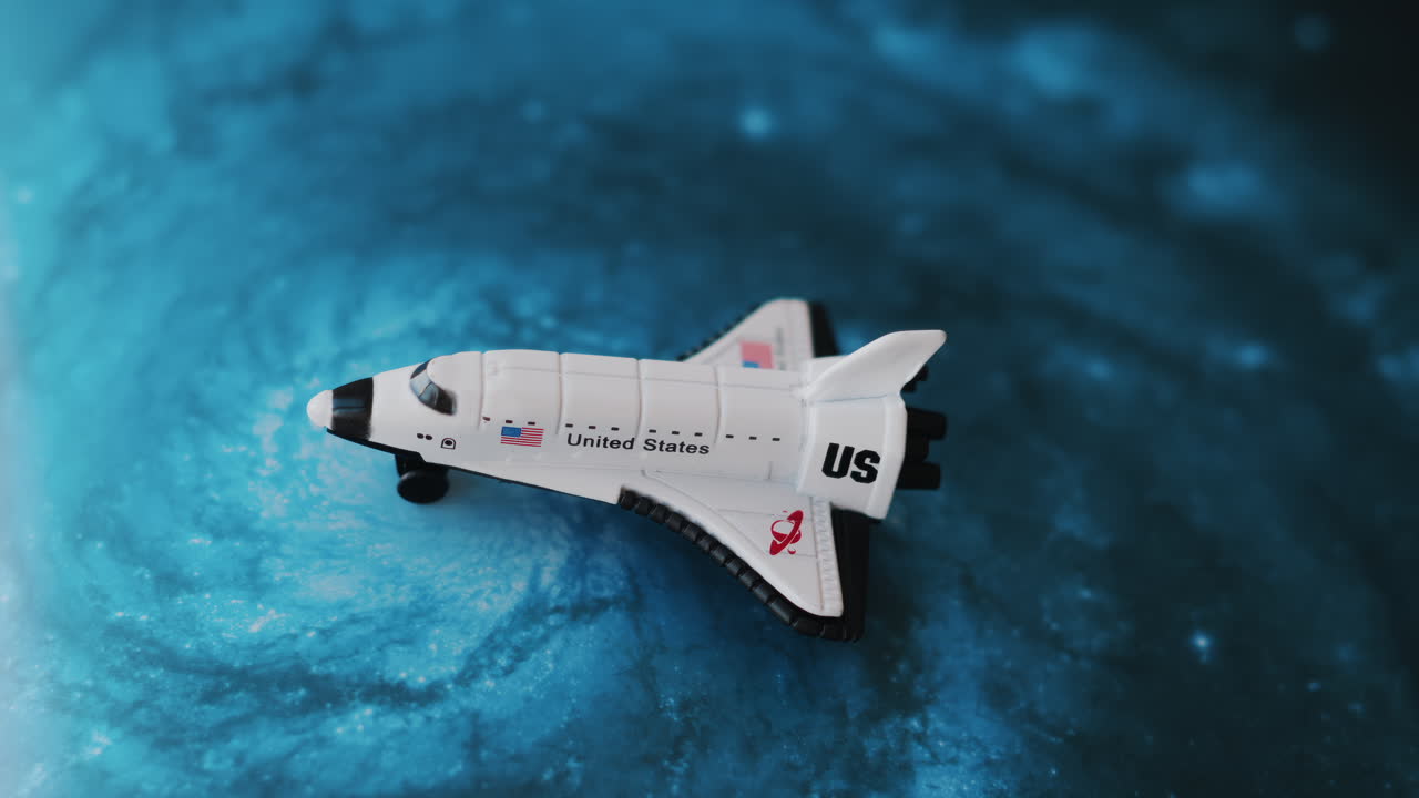 Close up of a miniature toy space shuttle placed on a blue cosmic galaxy backdrop
