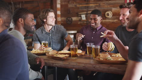 amigos hombres bebiendo cerveza y comiendo hamburguesas en un bar deportivo.