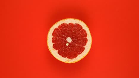 top view: half of an grapefruit rotates on a red surface - slow motion