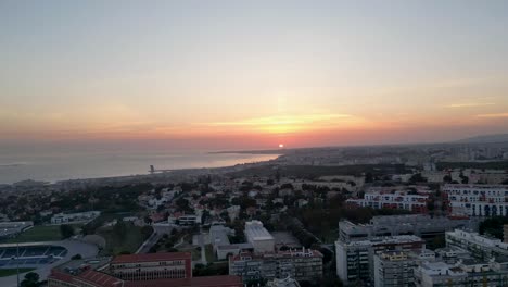 Aerial-view-of-sunset-cast-its-warm-hues-over-the-picturesque-city-of-Lisbon-and-its-vibrant-marine-surroundings-in-Portugal,-epitomizing-the-beauty-and-allure-of-coastal-landscapes