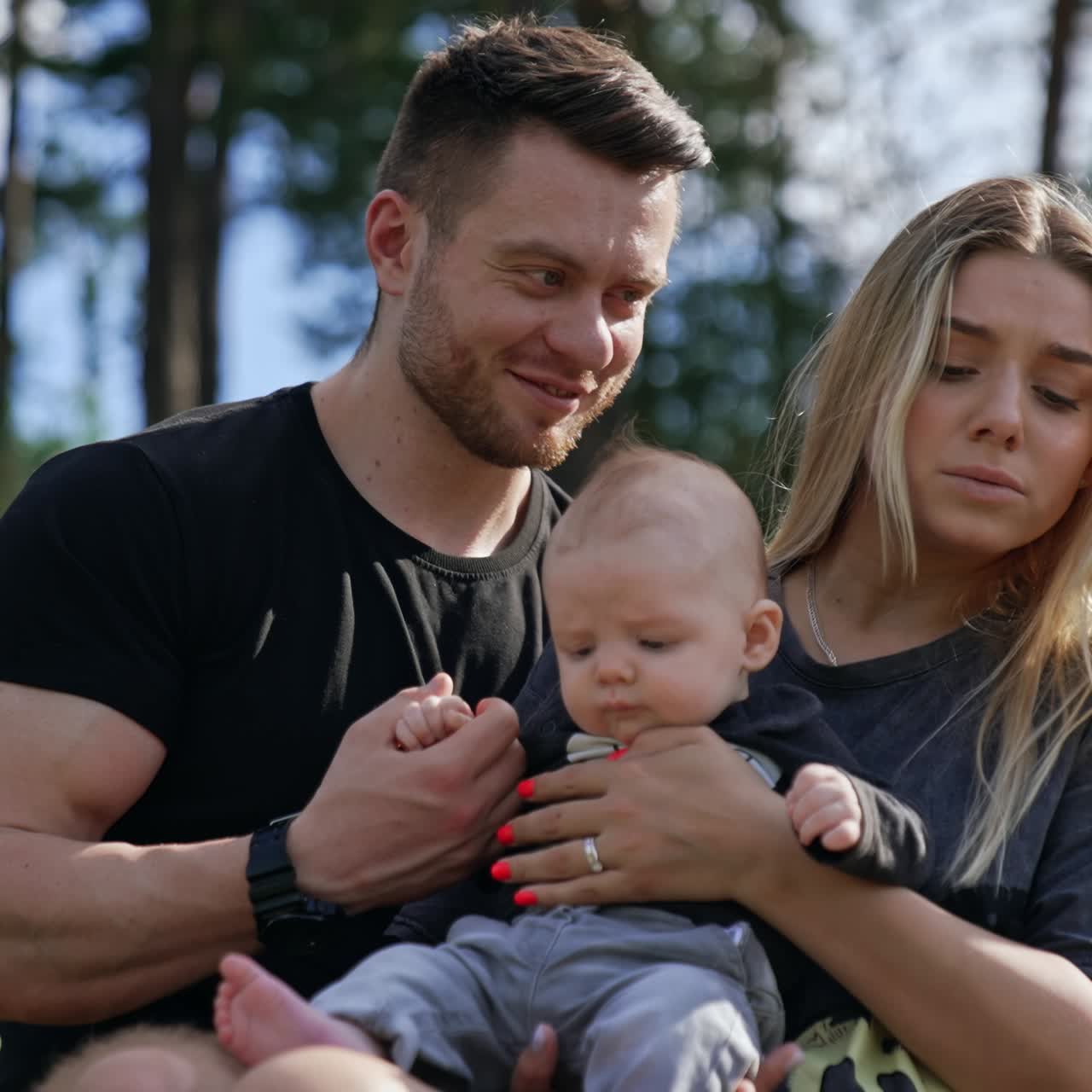 Adorable blonde newborn is held by his loving parents. Happy family having leisure time in nature on sunny summer day