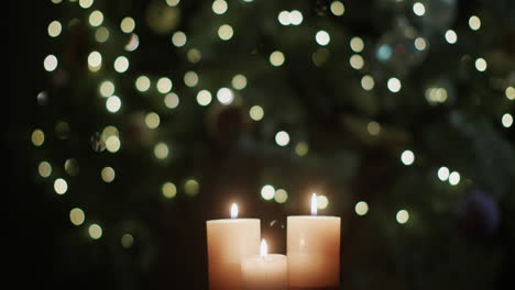 tres velas arden con el telón de fondo de las luces borrosas del árbol de navidad.