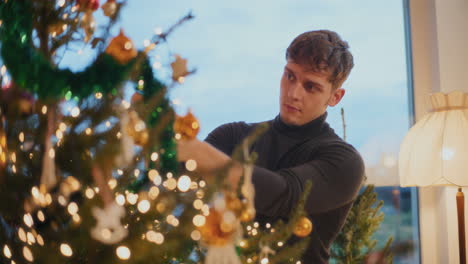 man decorating xmas tree with bauble at home