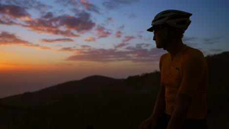 a man standing on a bicycle atop the mountain gazes at the sunset while the camera glides on a steadicam