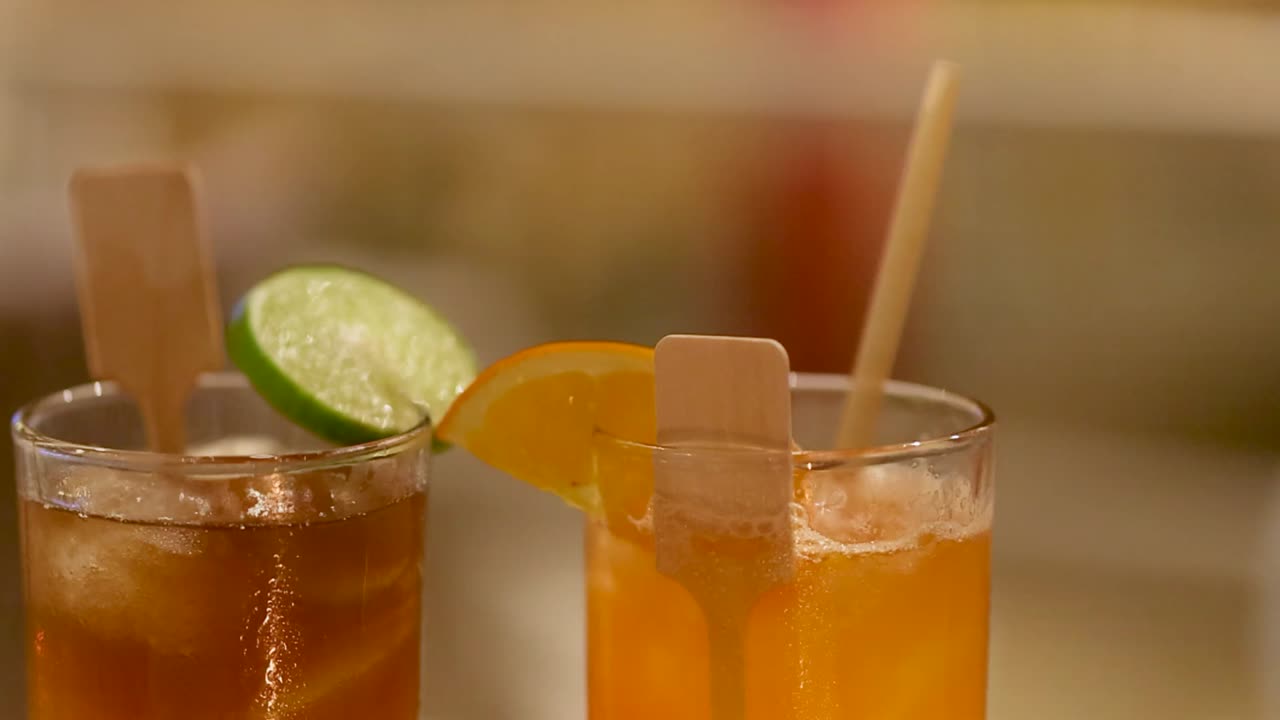 Una mano si protende per prendere cocktail ghiacciati colorati guarniti con lime e arancia.