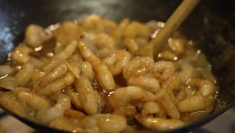 prawns being stirred in sauce inside wok with wooden spoon