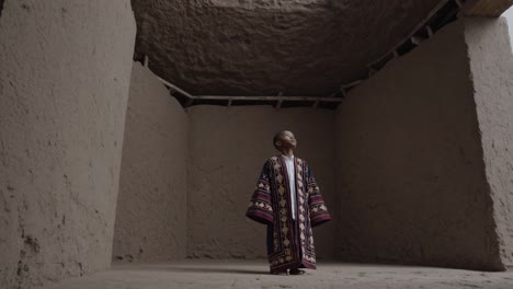 young boy wearing traditional clothing stands inside an ancient mud brick building. gazing upwards with a sense of wonder and reverence. capturing a moment of reflection and connection to heritage