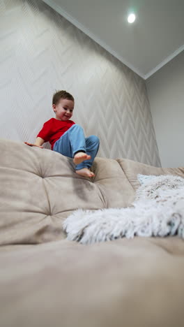 active caucasian kid plays on the sofa. toddler climbs and jumps on the furniture. low angle view. vertical video.