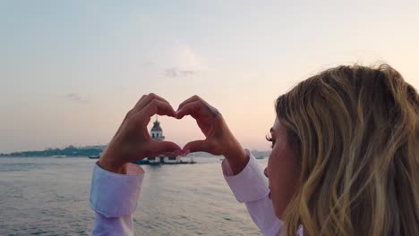 Slow-Motion:Beautiful-girl-makes-heart-shape-with-view-of-Maiden-Tower-inside-in-Istanbul,-Turkey