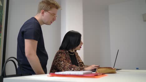 man explaining problem to woman working on laptop