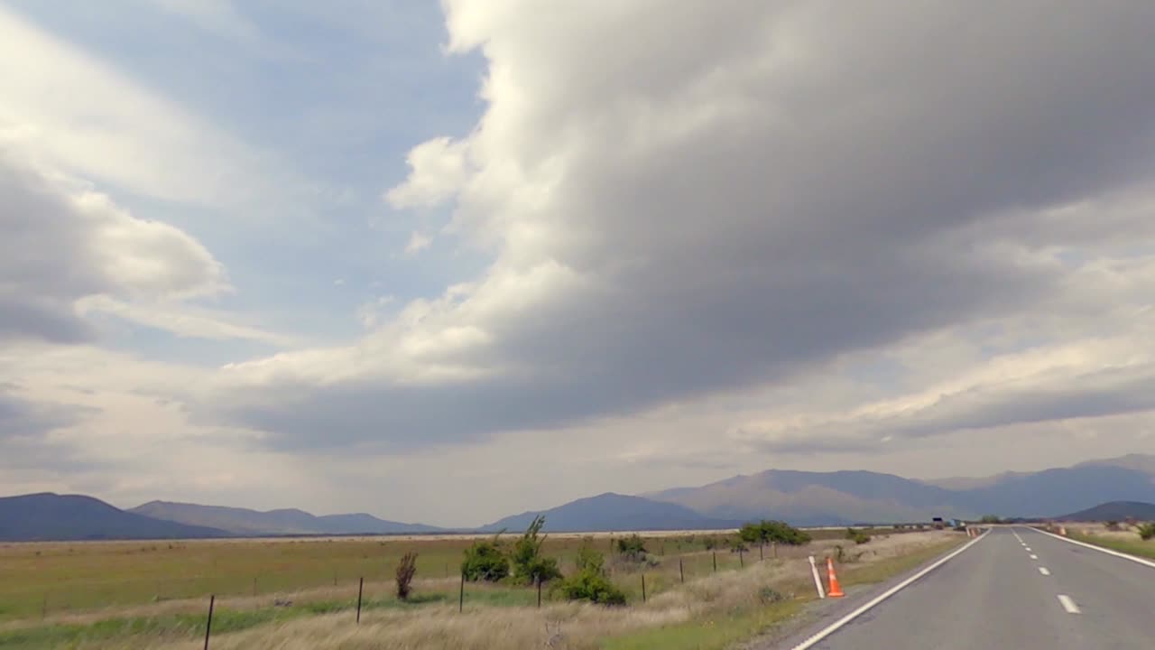 Panoramic view of open fields and mountain range in the background while on a road trip (slow motion)
