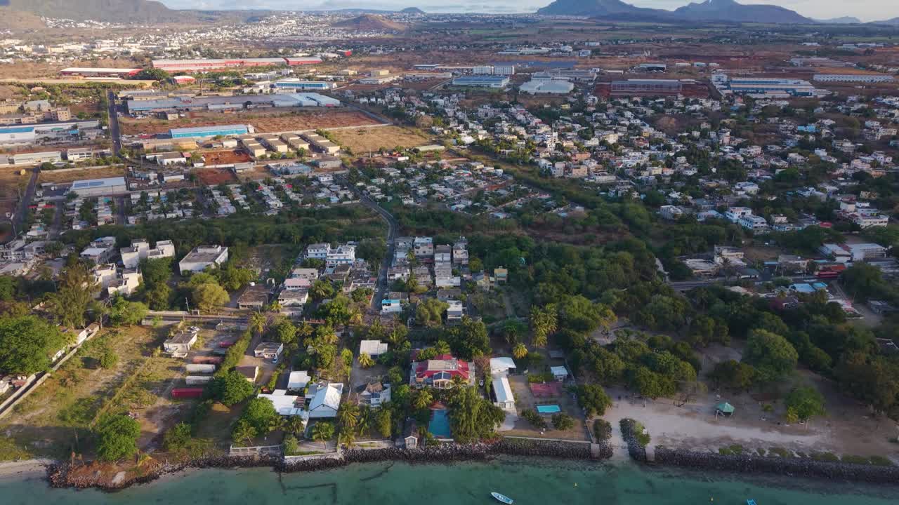 Aerial view of a coastal resort near Port Louis, Mauritius, at sunset. Scenic tropical shoreline with palm trees, villas, and calm turquoise water captured in UHD