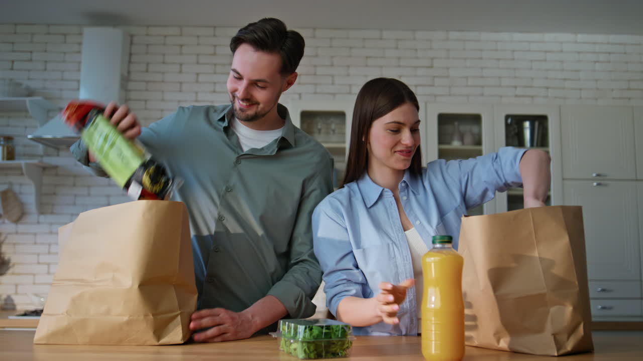 Shopping couple entering kitchen unpacking groceries in white interior closeup