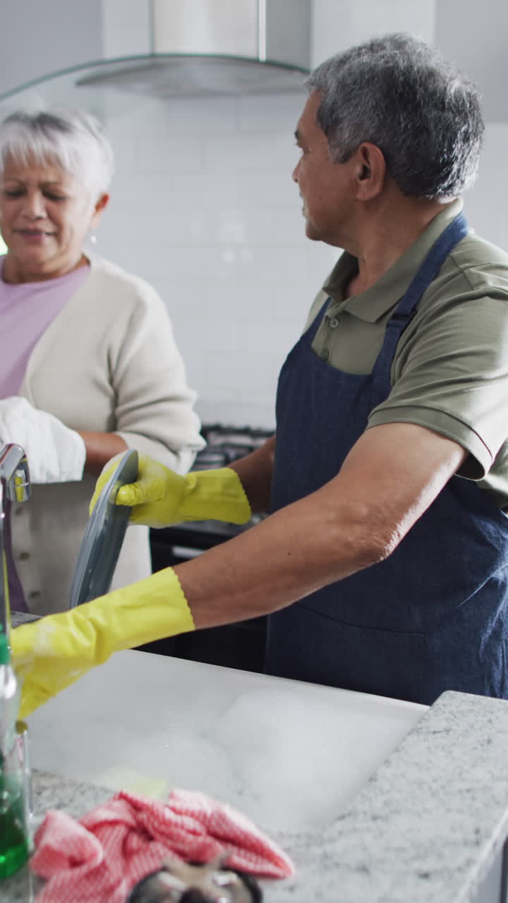 Vertical video of happy senior biracial couple washing dishes
