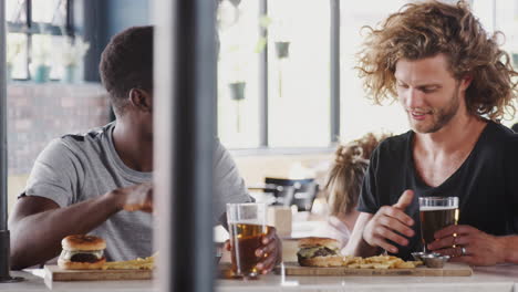 two male friends eating food and drinking beer in sports bar