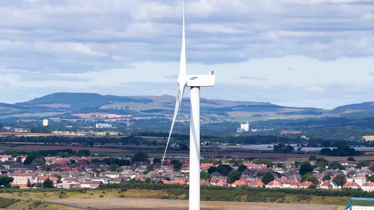 Large wind turbine slowly rotates above Dundee rooftops, bright daylight, wide landscape view