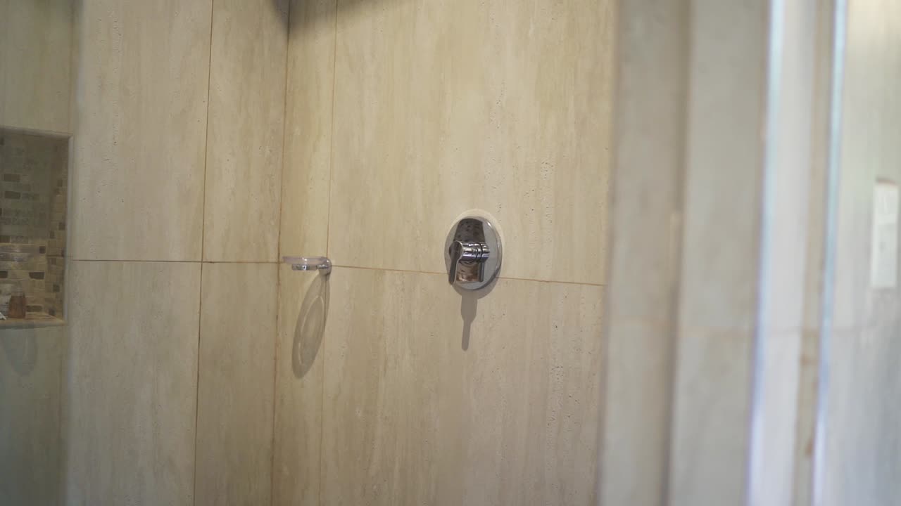Minimalist shower head fixture attached on a clean ceramic hotel bathroom wall, Argentina.