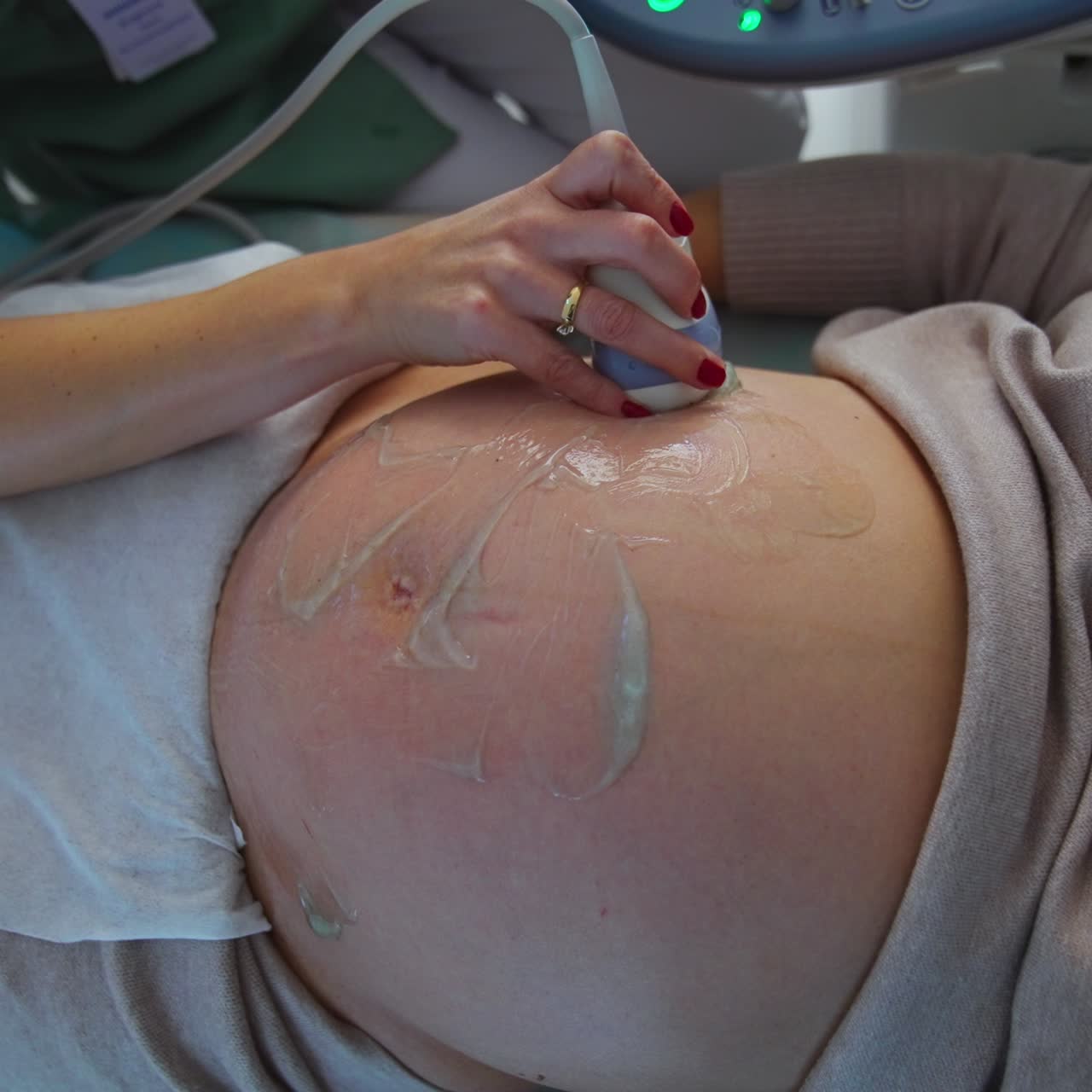 Mano del medico che tiene una sonda ecografica appoggiata su una grande pancia di donna incinta scoperta. Primo piano. Vista dall'alto.