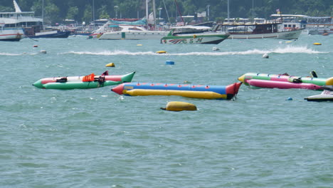 a speedboat moving to the right as banana boats are seen floating with a jet ski on the right, also yachts and other kinds of water vehicles are seen at the background, pattaya, thailand